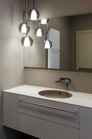 Stylish brown sink, chrome faucet, large mirror and ceiling light three-lamp chandelier. Modern bathroom design. Vertically framed shot.の写真素材