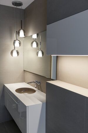 Stylish brown sink, chrome faucet, large mirror and ceiling light three-lamp chandelier. Modern bathroom design. Vertically framed shot.の写真素材