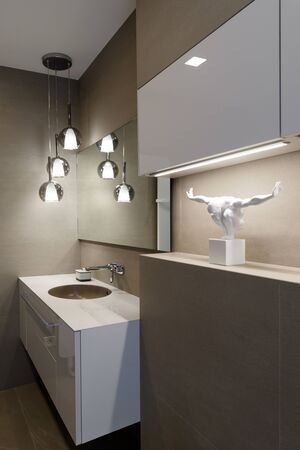 Stylish brown sink, chrome faucet, large mirror and ceiling light three-lamp chandelier. Shelf with statuette. Modern bathroom design. Vertically framed shot.の写真素材