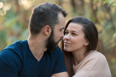 Portrait of young beautiful couple in the Park. They look at each other. In the background of leaves of trees. Horizontally framed shot.の写真素材