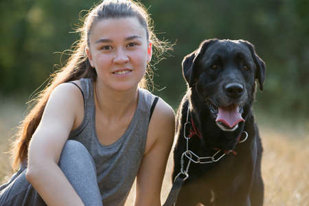 Young attractive sport girl with black Labrador in park. Healthy lifestyle. Walk with favorite pet...