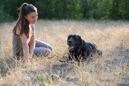 Young attractive sport girl with black Labrador in park. Healthy lifestyle. Walk with favorite pet in wood. Horizontally framed shot.の写真素材