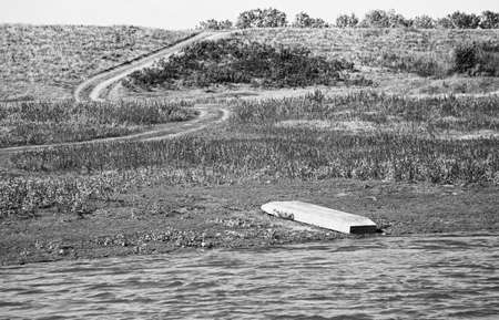 Overturned boat on the river Bank. The trail goes into the distance. Horizontally framed shot.の写真素材