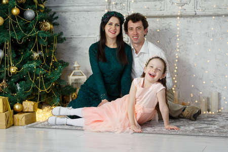 Young happy family at the Christmas tree. Parents and their daughter celebrate the new year. New Year room. Christmas good mood. Lifestyle, family and holiday. Horizontally framed shot.の写真素材
