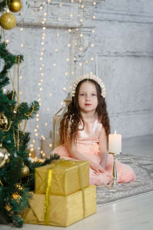 Little cute girl sitting at the Christmas tree. New Year room. Christmas good mood. Lifestyle, family and holiday. Vertically framed shot.の写真素材