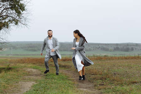 A mischievous couple of newlyweds are running around and having fun in the countryside. Happy moments of the wedding day. Horizontally framed shot.の写真素材