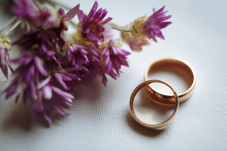 Two golden wedding rings and pink flowers on white background. Horizontally framed shot.の写真素材