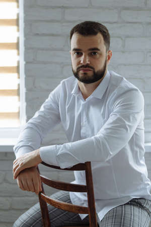 Portrait of a smart serious young man sitting on a chair. Vertically framed shot.の写真素材
