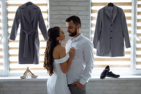 Bride and groom embrace on background of wedding costumes. Preparation for wedding. Horizontally framed shot.の写真素材