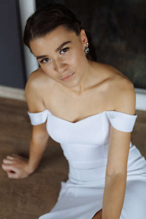 Portrait of an attractive young bride. Women in a wedding dress is sitting on the floor. Vertically framed shot.の写真素材