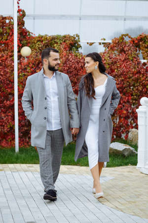 Stylish couple in gray coats walking in the autumn park. Happy sensual wedding couple. Romantic moments of newlyweds. Vertically framed shot.の写真素材