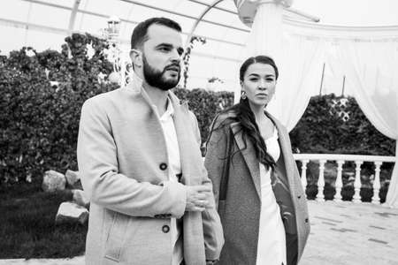 Stylish couple in gray coats walking in the autumn park. Happy sensual wedding couple. Romantic moments of newlyweds. Horizontally framed shot.の写真素材