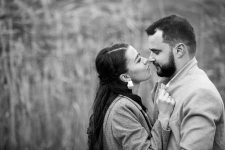 Stylish couple in gray coats gently hugging on the background of reeds. Happy sensual wedding couple embracing. Romantic moments of newlyweds. Horizontally framed shot.の写真素材