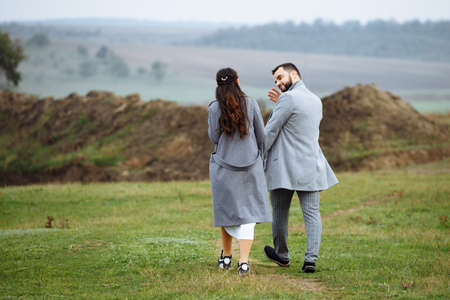 A stylish couple in gray coats walk through the countryside. Rear view. Horizontally framed shot.の写真素材