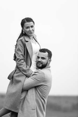 Stylish couple in gray coats on the background of nature. Groom lifts bride up. Happy moments of the wedding day. Vertically framed shot.の写真素材