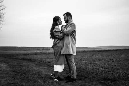 Stylish couple in gray coats gently hugging on the background of nature. Happy sensual wedding couple embracing. Romantic moments of newlyweds. Horizontally framed shot.の写真素材