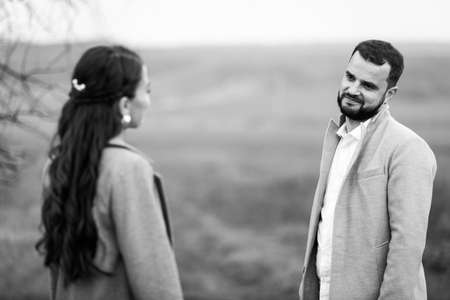 Stylish couple in gray coats on the background of nature. They look at each other. Horizontally framed shot.の写真素材