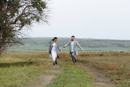 A mischievous couple of newlyweds are running around and having fun in the countryside. Happy moments of the wedding day. Horizontally framed shot.の写真素材