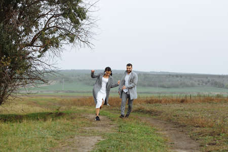 A mischievous couple of newlyweds are running around and having fun in the countryside. Happy moments of the wedding day. Horizontally framed shot.の写真素材