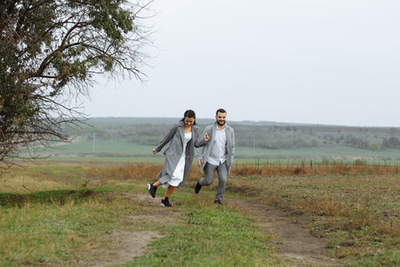 A mischievous couple of newlyweds are running around and having fun in the countryside. Happy moments of the wedding day. Horizontally framed shot.の写真素材