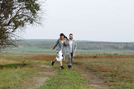 A mischievous couple of newlyweds are running around and having fun in the countryside. Happy moments of the wedding day. Horizontally framed shot.の写真素材
