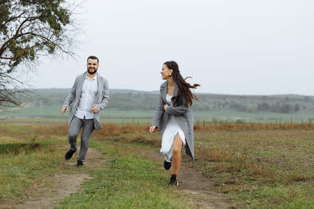 A mischievous couple of newlyweds are running around and having fun in the countryside. Happy moments of the wedding day. Horizontally framed shot.の写真素材