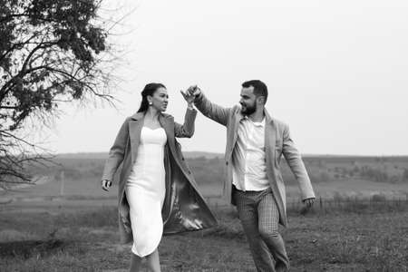 Cheerful couple of newlyweds are walking through the countryside. Groom circles bride. Happy moments of the wedding day. Horizontally framed shotの写真素材
