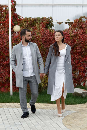 Stylish couple in gray coats walking in the autumn park. Happy sensual wedding couple. Romantic moments of newlyweds. Vertically framed shot.の写真素材