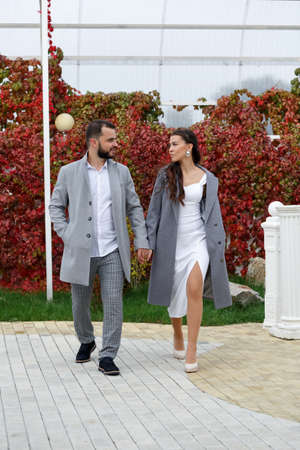 Stylish couple in gray coats walking in the autumn park. Happy sensual wedding couple. Romantic moments of newlyweds. Vertically framed shot.の写真素材