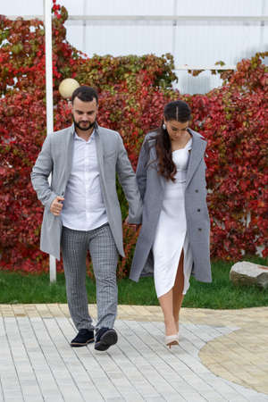 Stylish couple in gray coats walking in the autumn park. Happy sensual wedding couple. Romantic moments of newlyweds. Vertically framed shot.の写真素材