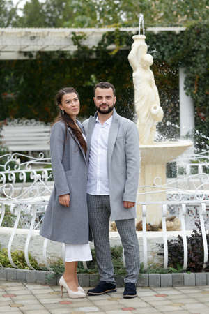 Stylish couple in gray coats walking in the autumn park. Happy sensual wedding couple. Romantic moments of newlyweds. Horizontally framed shot.の写真素材
