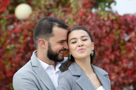 Stylish couple in gray coats gently hugging on the background of autumn leaves. Happy sensual wedding couple embracing. Romantic moments of newlyweds. Horizontally framed shot.の写真素材