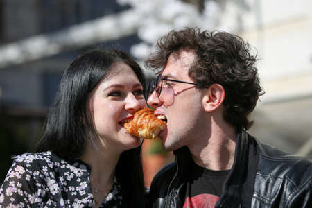 Happy young couple in morning and having breakfast. Cheerful man and woman bite a croissant at the same time. Horizontally framed shot.の写真素材