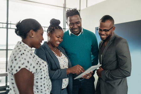 Team of african business people standing and smiling and laughing while using a tabletの写真素材