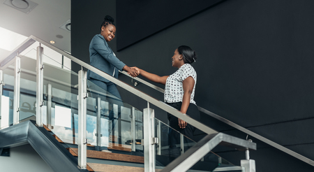 Executive african american woman shaking hands with welcoming smile on a staircaseの写真素材