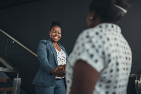 Executive african american woman shaking hands with welcoming smile on a staircaseの写真素材