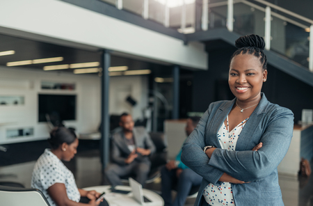 Portrait of a confident black businesswoman smiling with her arms crossed and all african team in the backgroundの写真素材
