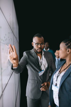 Black african businessman looking at female colleague pointing to large video screen for a presentation during a conference.の写真素材