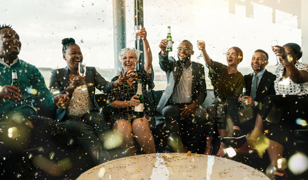 A festive multi ethnic group of people smiling, toasting with sparkling wine and beer. Celebrating the end of the working year and to the new year ahead