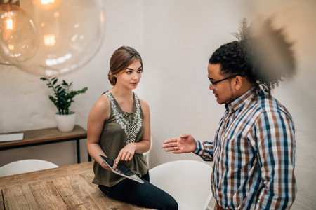 Two young creatives talking and using tablet in boardroom, the woman is pointing to a tablet and the mixed race guy is explainingの写真素材