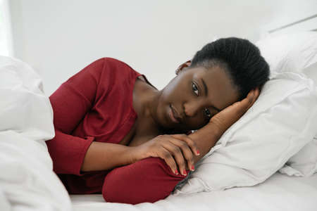 Close up portrait of beautiful Black African woman laying on bed, feeling depressed and anxious.の写真素材