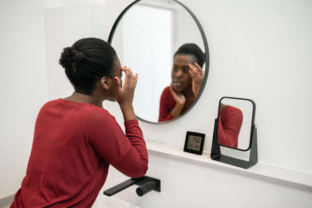 Beautiful Black African woman looking at her face in the bathroom mirror. Part of her morning self care routineの写真素材