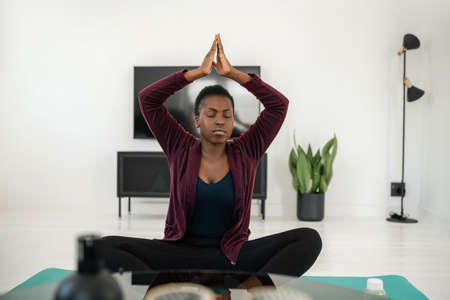 Close up of black African woman sitting in yoga pose on mat in living room, Stretching and meditation at home work outの写真素材
