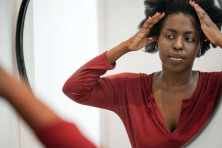Mourning routine of Black African woman fixing her hair and looking into bathroom mirror. Hair styling and getting readyの写真素材