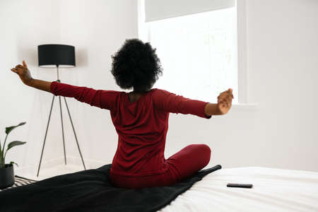 Behind view, early morning routine of beautiful African Woman stretching arms outwards while sitting...
