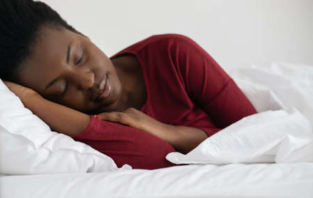 Young beautiful African woman sleeping in white linen bed, wearing red pajamas.の写真素材
