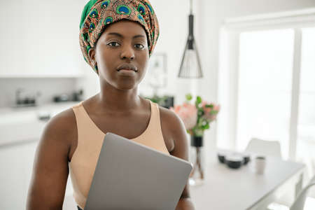 Close up Portrait of a confident African woman with her arms crossed looking into the camera. Working from home and wearing a traditional headscarfの写真素材