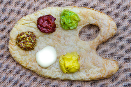 Tasty and colourful sauces and relishes on a puff pastry artist's palette - guacamole, tomato, wholegrain dijon mustard, mayonnaise and mustard.の写真素材