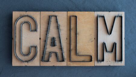 Old wood and steel number plate dies spell out the word CALMの写真素材