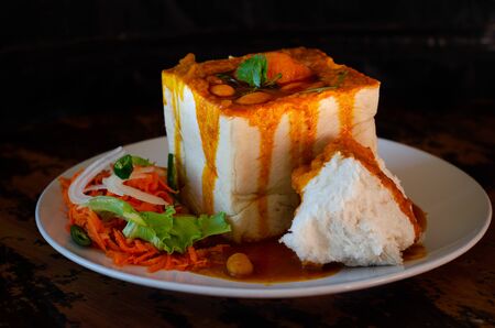 A Durban Bunny Chow - or, in this case, a vegerarian quarter bean bunny - served with sambals. This is an iconic Durban meal consisting of a section of a loaf of bread hollowed out and filled with bean curry and gravy. The sambals are grated carrot with chopped chilli. The meal is traditionally eaten with one's fingers.の写真素材